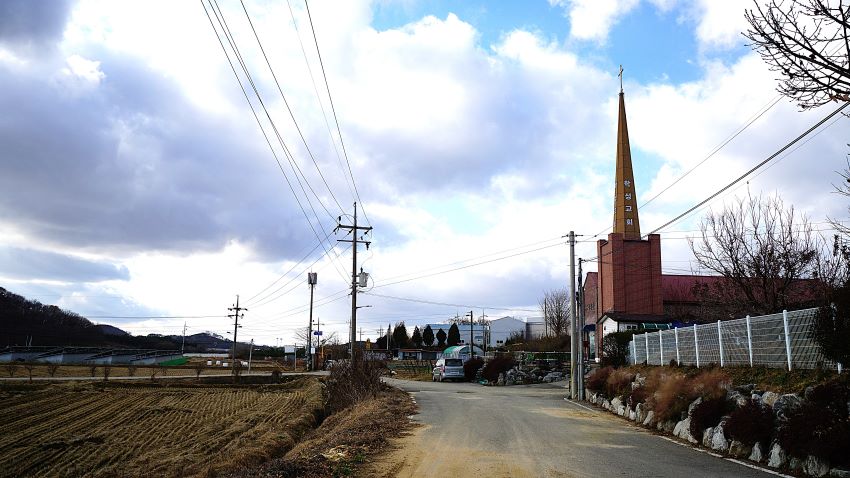 우측에 뾰족한 학성교회 건물, 푸른 하늘, 흰구름, 왼쪽에 들판, 가운데 전신주, 세로로 늘어진 전깃줄,