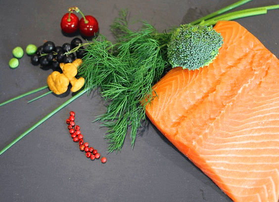 주황색 연어살을 가진 생 연어 조각이 있고, 왼쪽에는 발간 체리 2개, 검정 올리브 한덩이, 로즈마리와 브로콜리가 있다.