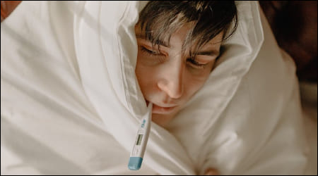 감기에 걸려 이불을 뒤집어 쓰고 체온계를 입에 문 남자