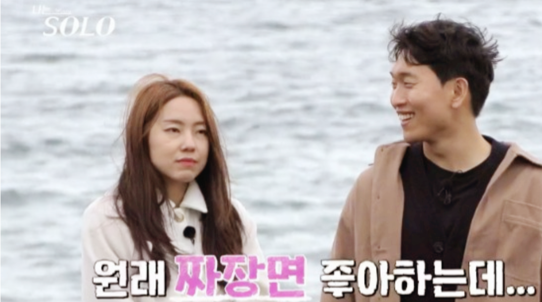 나솔- 바다를 배경으로 흰쟈켓을 입고 무표정한 현숙과 베이지 쟈겟을 입고 현숙을 바라보며 웃는 남자