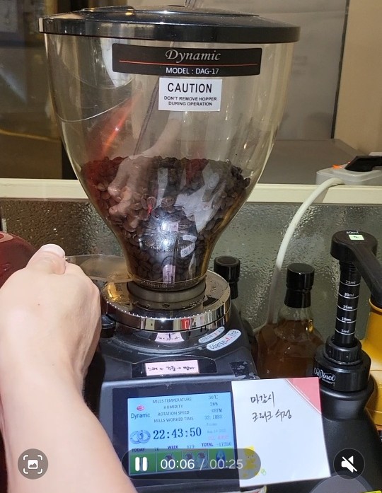 카페 그라인더 본체에 부착된 사장이 직접 제작한 '조작 주의사항'과 '분쇄도 조절 가이드' 스티커 사진. 말로 하는 교육 대신 시각화된 매뉴얼을 통해 초보 알바생의 실수를 줄이고 예방 정비를 유도하는 자산 관리 전략을 보여줌.