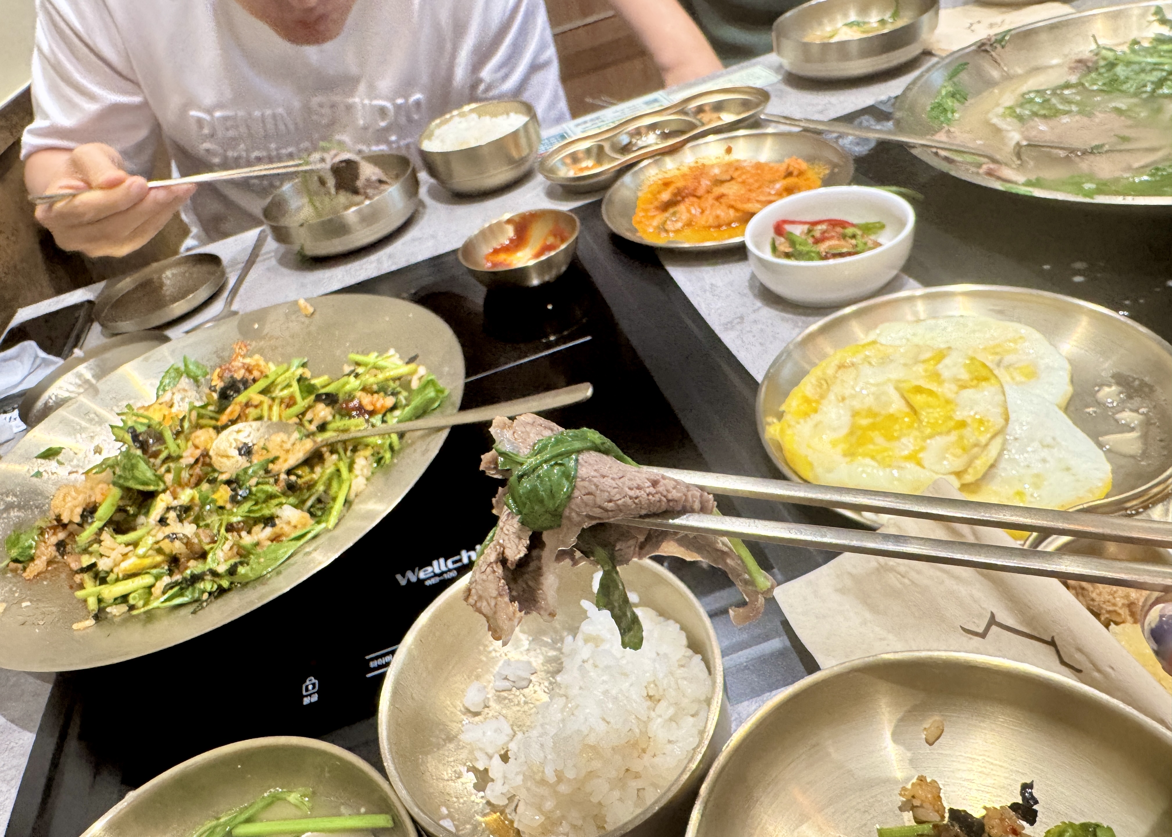 숟가락 위 도톰한 소고기와 미나리&amp;#44; 뒤로 미나리 비빔밥이 보이는 클로즈업