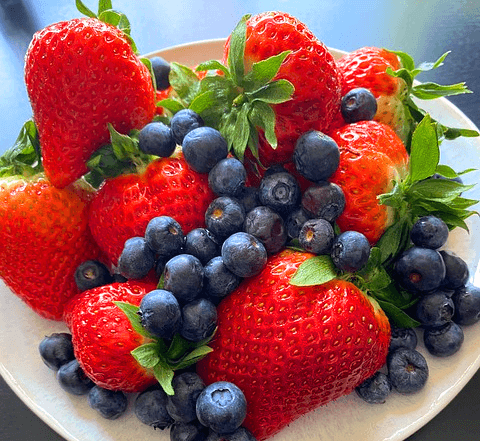 하얀 접시에 빨간 딸기들과 보라색 블루베리들이 가득 담겨있다.