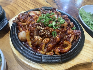 옅은-갈색-밑-받침과-검정색-주물-팬에-올려있는-주꾸미-메뉴