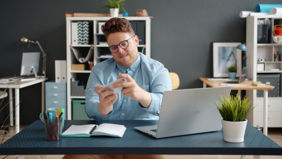 Smiling man using smartphone at a desk in a modern office.