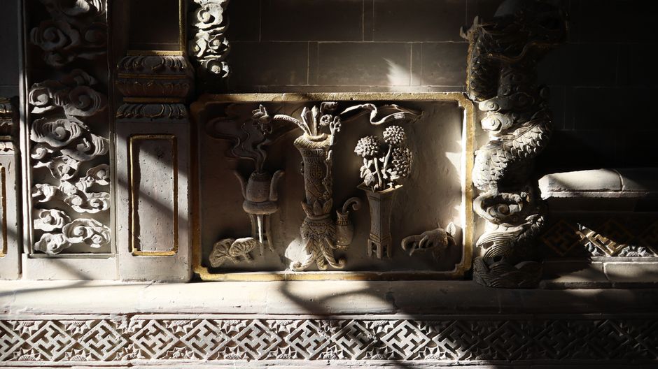 Intricate stone carving with floral and dragon motifs illuminated by sunlight in a temple.