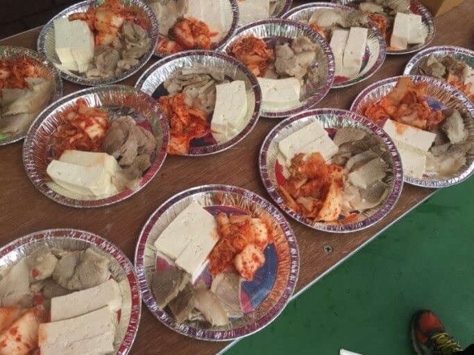 나무 책상 위에 놓인 접시에 담긴 수육과 두부, 김치