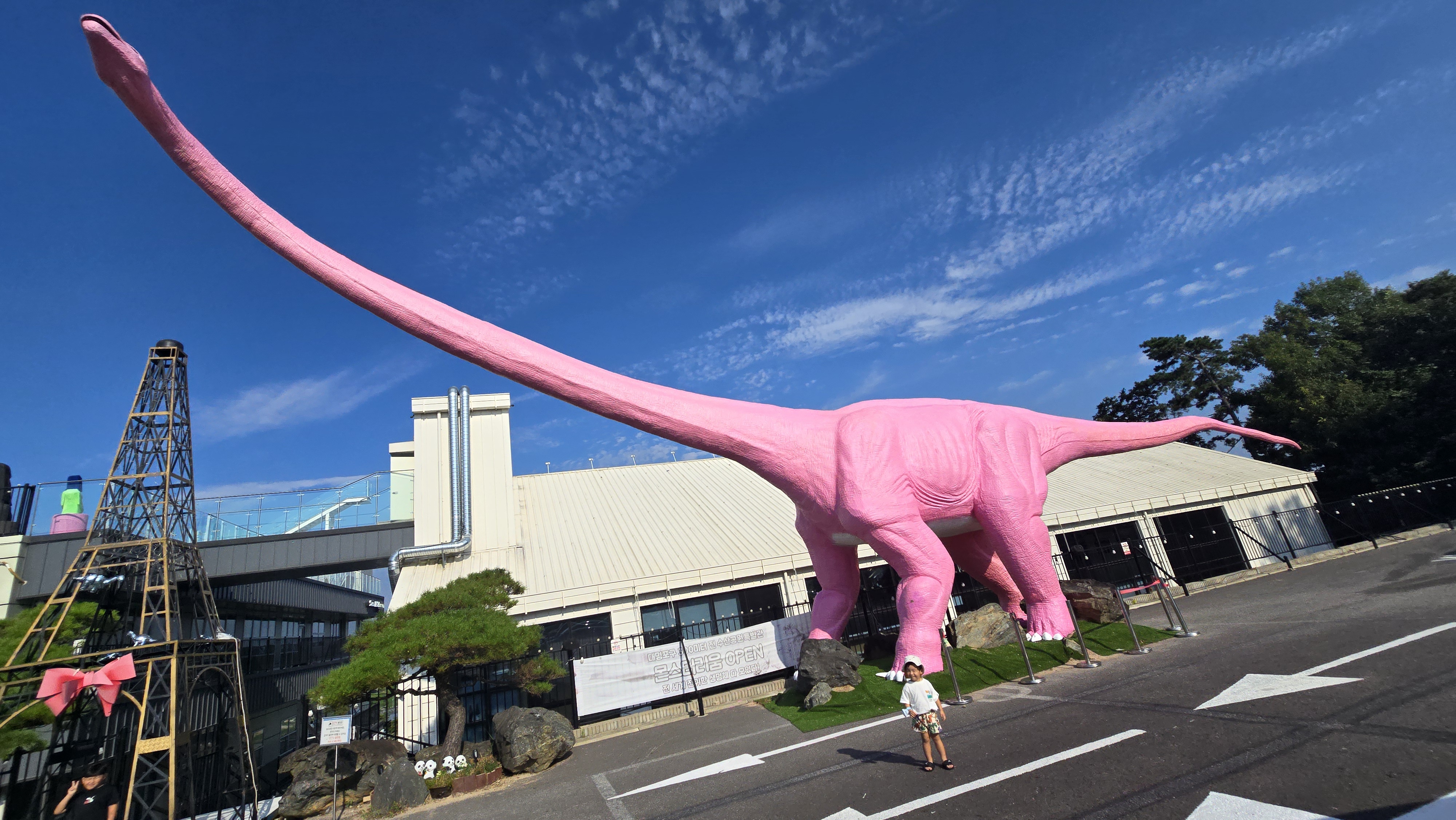 김포 수산공원 쥬라기존에 설치된 분홍색 브라키오사우루스 조형물과 그 앞에 선 어린이의 모습