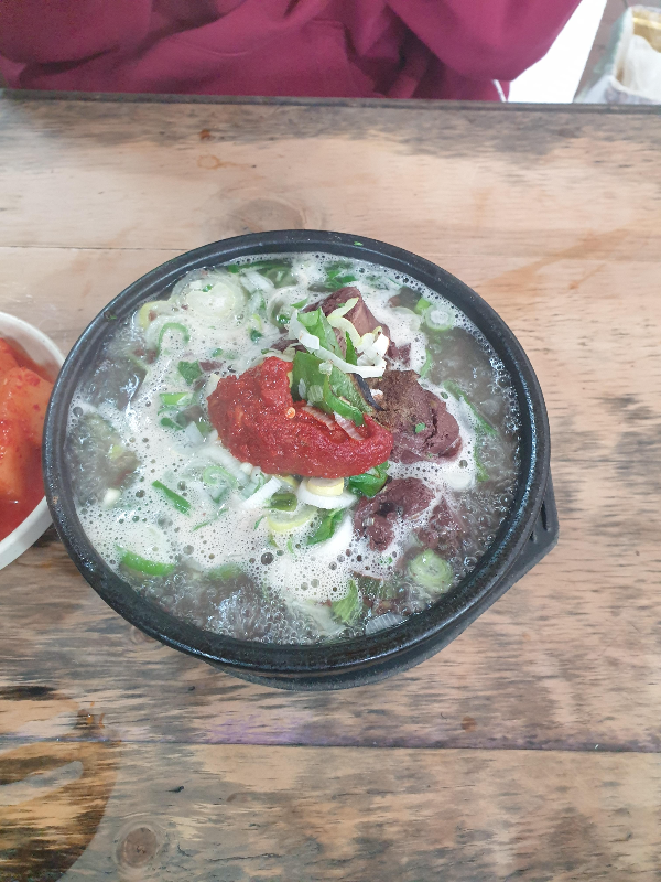 테이블 위에 순대국밥이 올려져있다. 순대 국밥에 붉은 다진 양념이 올려져있다.