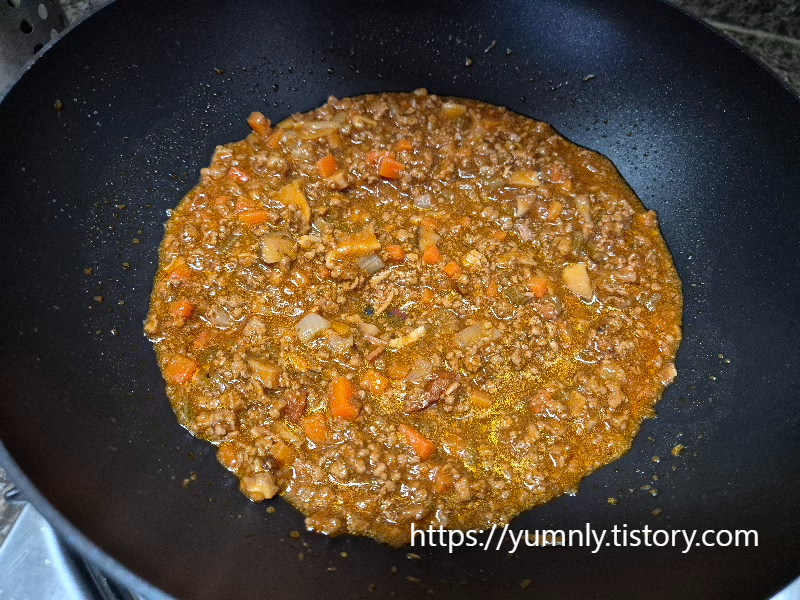 Adding two and a half ladles of ragu sauce into a frying pan