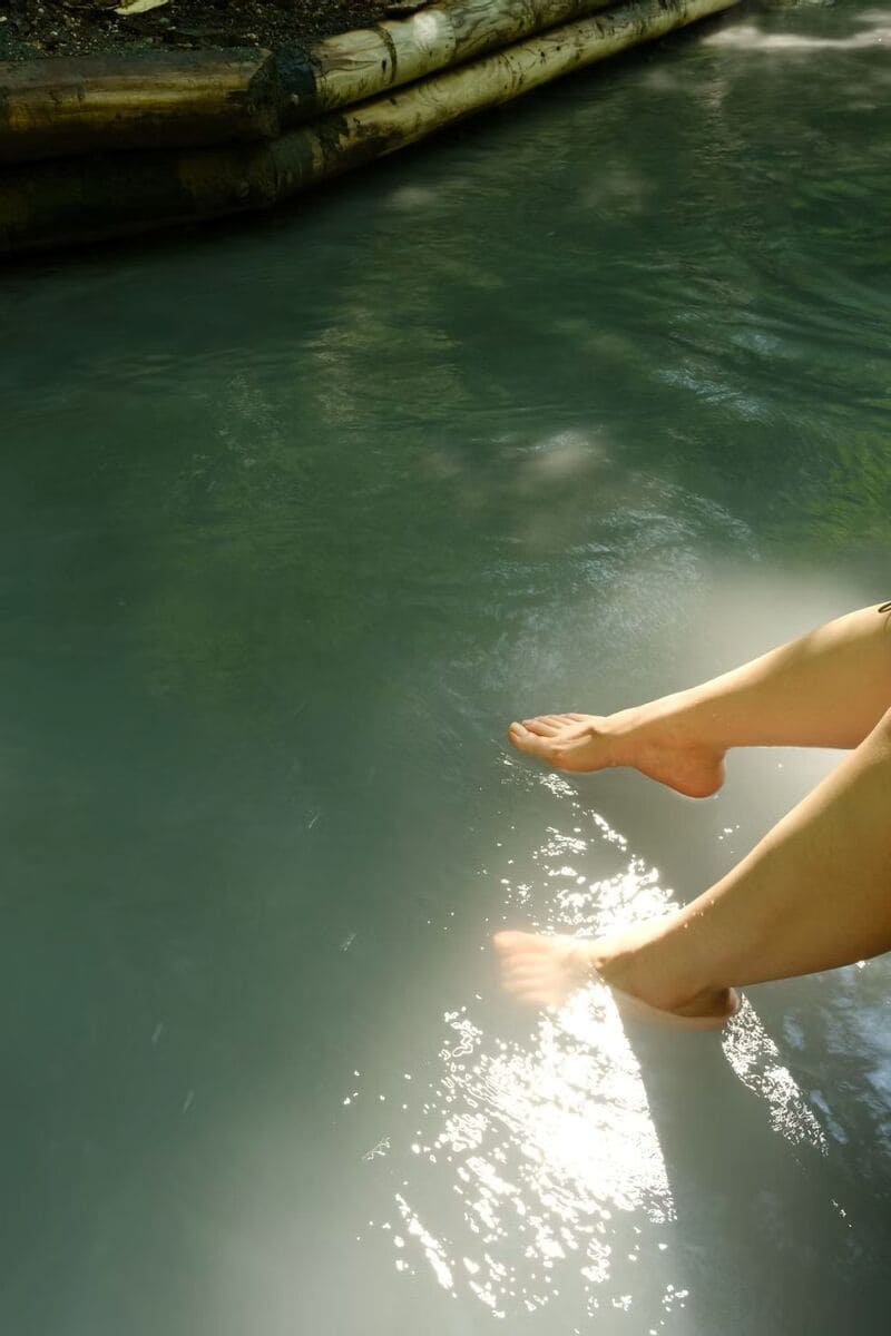 노보리베츠 온천 거리에서 족욕을 즐기는 모습, 햇살에 반짝이는 따뜻한 온천수 위에 발을 담근 장면