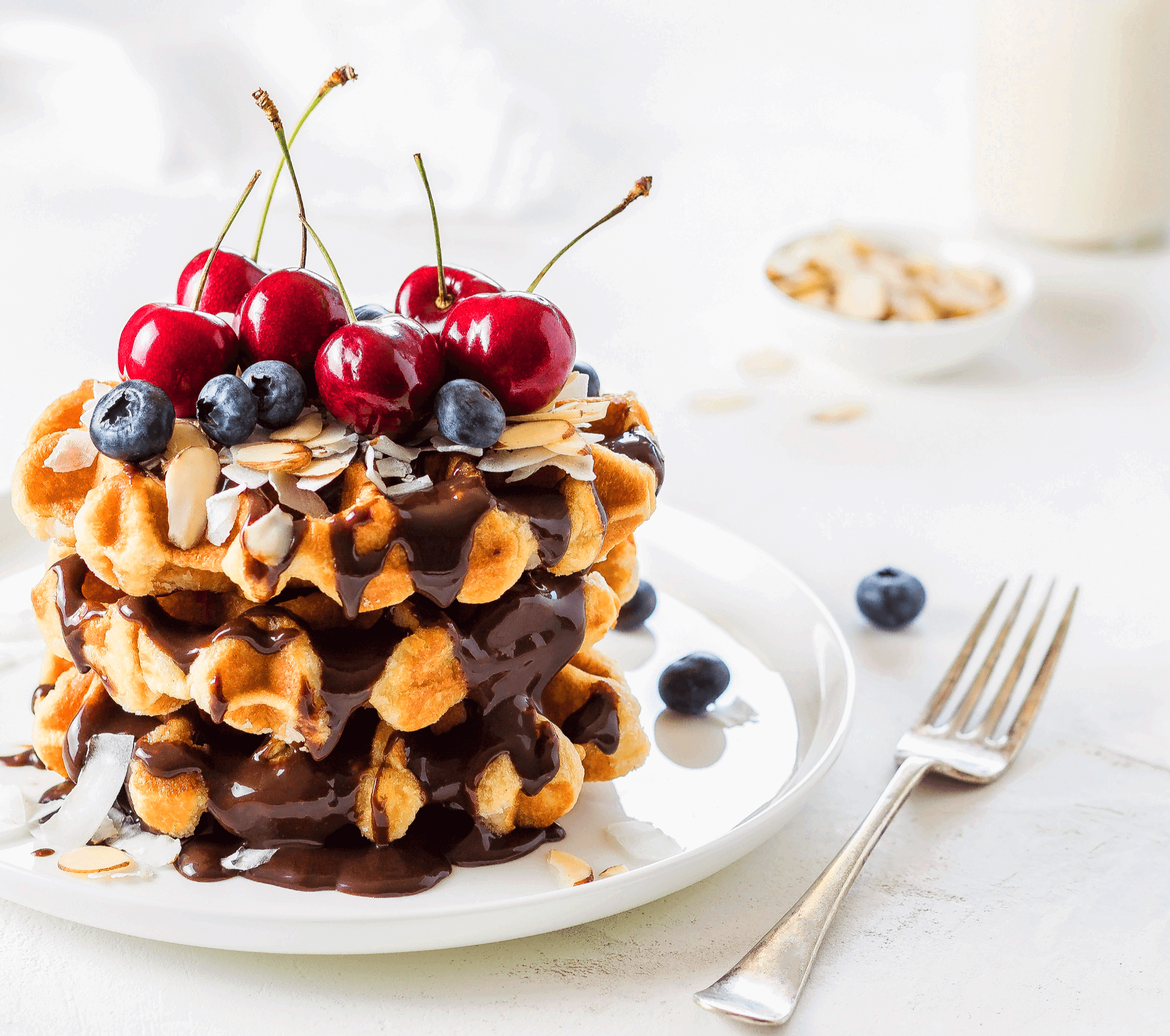 하얀 접시에 초콜릿 케이크가 있고 맨 위에는 빨간 체리들과 블루베리들이 있다.