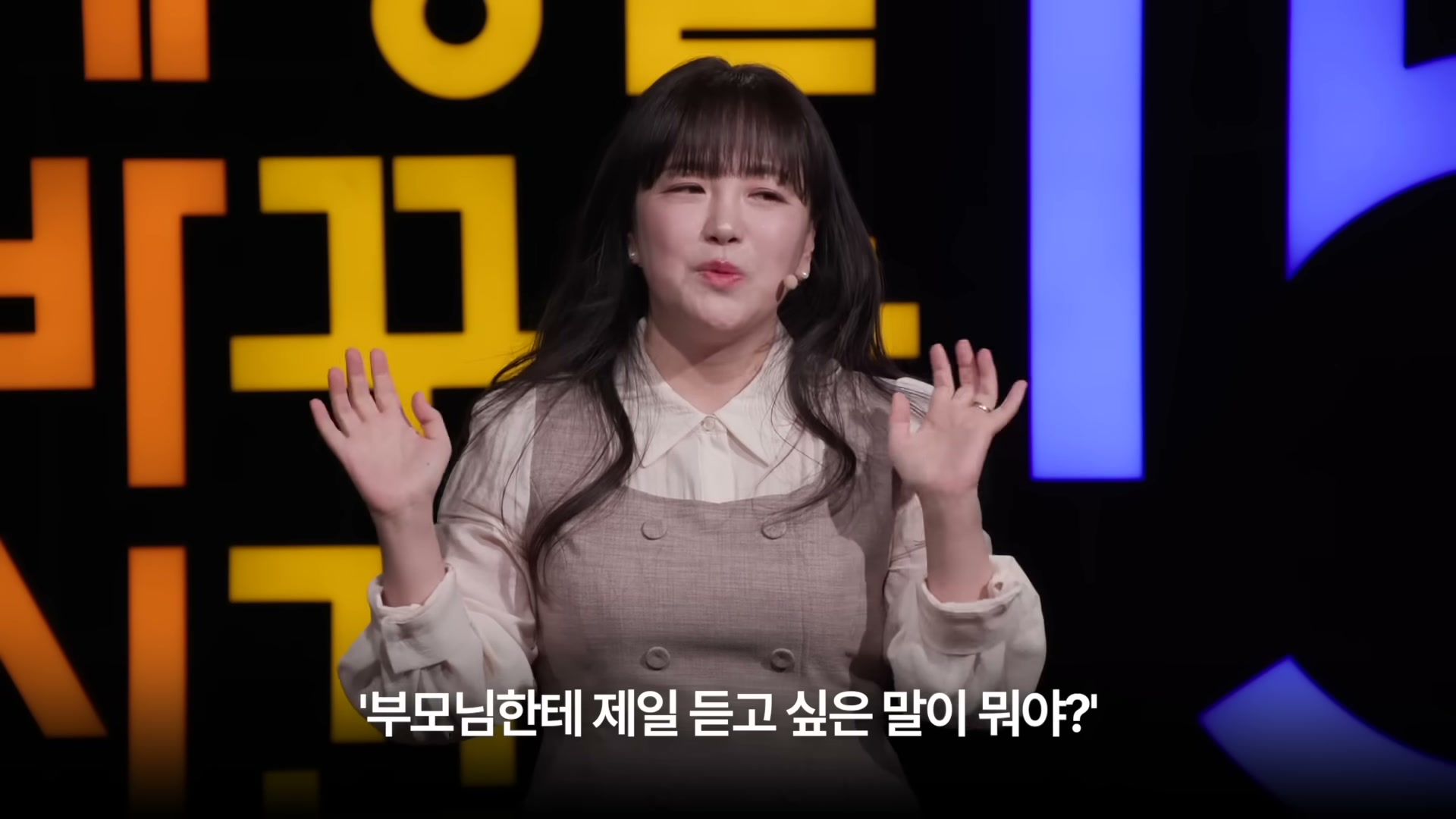 검은 무대 위 강연자 김민정이 양손을 펼친 모션, 하단 자막에 '부모님한테 제일 듣고 싶은 말이 뭐야?'