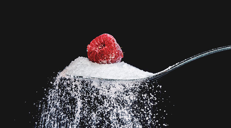 숫가락에 가득 담긴 설탕과 그 위에 얹힌 1개의 빨강색 베리