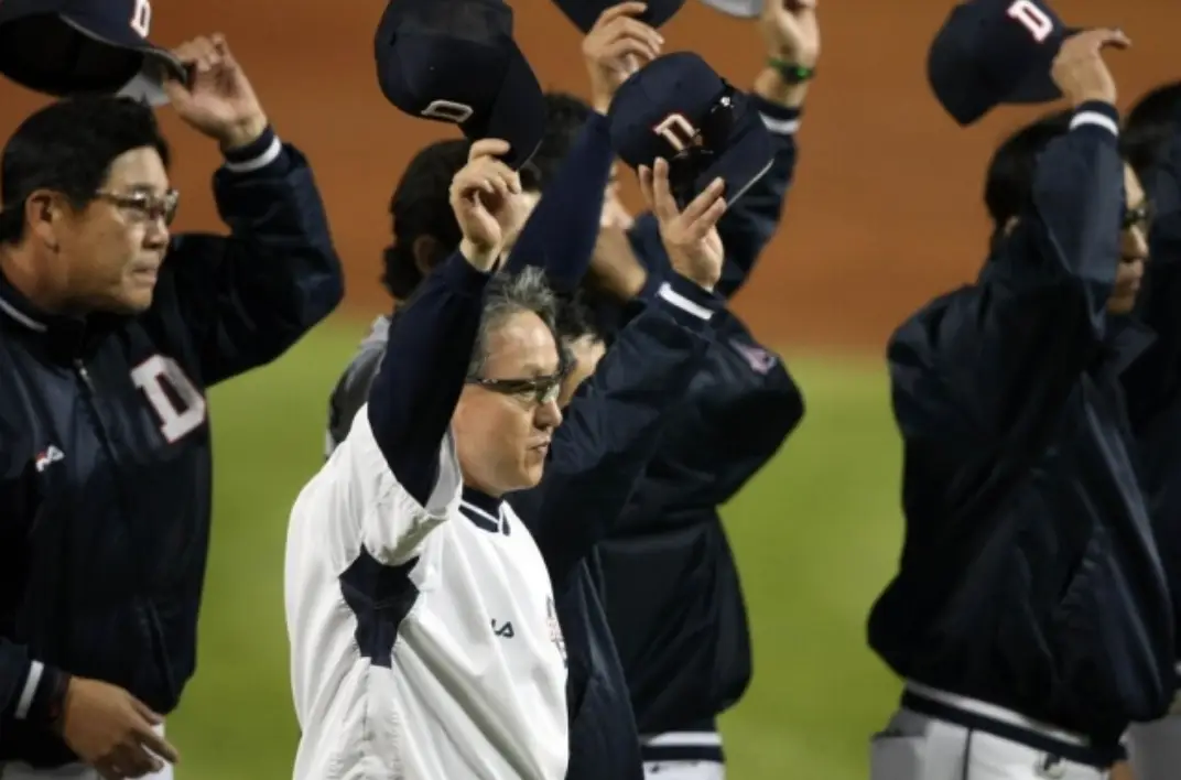 검은 옷을 입은 사람들 사이 흰옷을 입고 모자를 위로 든채 걷고있는 김경문 감독 옆모습