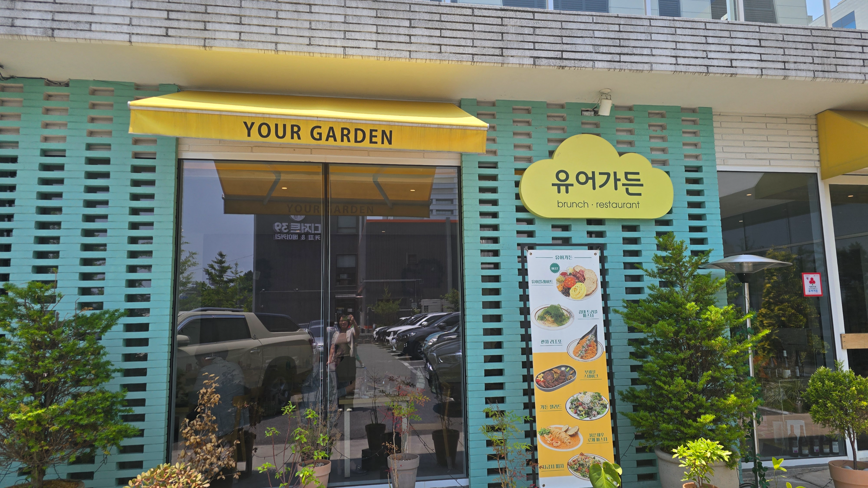 유어 가든(YOUR GARDEN) 브런치 레스토랑 외관,노란색 차양과 한국어 간판이 보이며, 입구에는 화분과 메뉴 판이 배치되어 있음