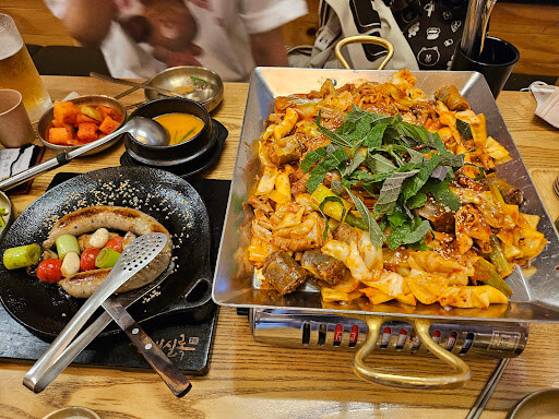 대학로 맛집 순대실록의 인기 메뉴&amp;#44; 철판 순대볶음과 소시지 플레이트. 상추와 깻잎이 곁들여져 있으며 술안주로도 인기 있는 메뉴.
