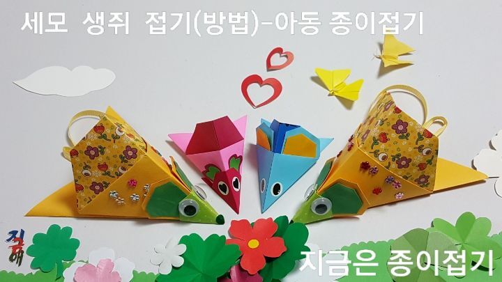 종이접기로 만든 세모 생쥐 네 마리가 꽃 향기를 맡으며 모여 있어요. 생쥐 접는 방법을 설명하며 만든 두 마리의 색종이 쥐와 꽃무늬가 있는 큰 종이로 만든 노란쥐 두 마리가 있어요.