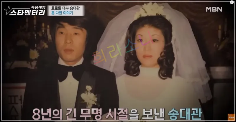 젊은 시절 송대관 부부의 결혼식 사진. 송대관은 검은 턱시도를 입고 있고&amp;#44; 아내는 하얀 웨딩드레스와 면사포를 착용한 모습. 화면에는 &amp;quot;8년의 긴 무명 시절을 보낸 송대관&amp;quot;이라는 자막이 있다.