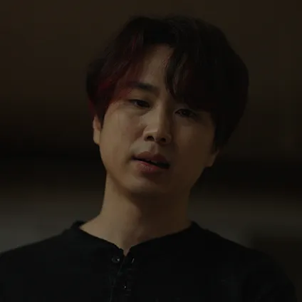 어두운 실내를 배경으로 검은 티에 빨강 머리를 하고 있는 반동우