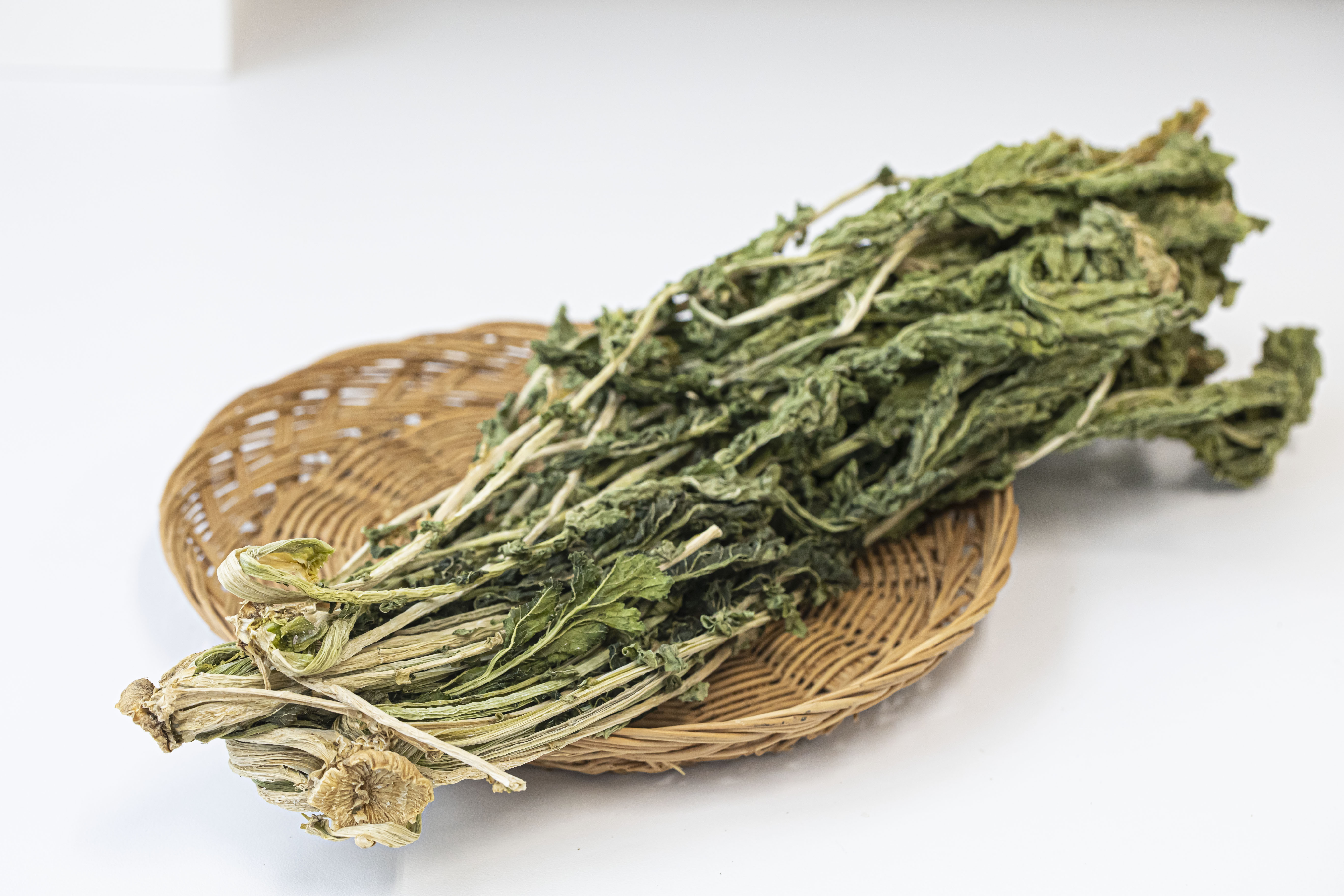 야생에서 채취를 한 무의 잎파리를 바싹 말린 우거지를 하얀 바닥 위에 동그란 대나무 받침대 위에 놓고 찍은 사진