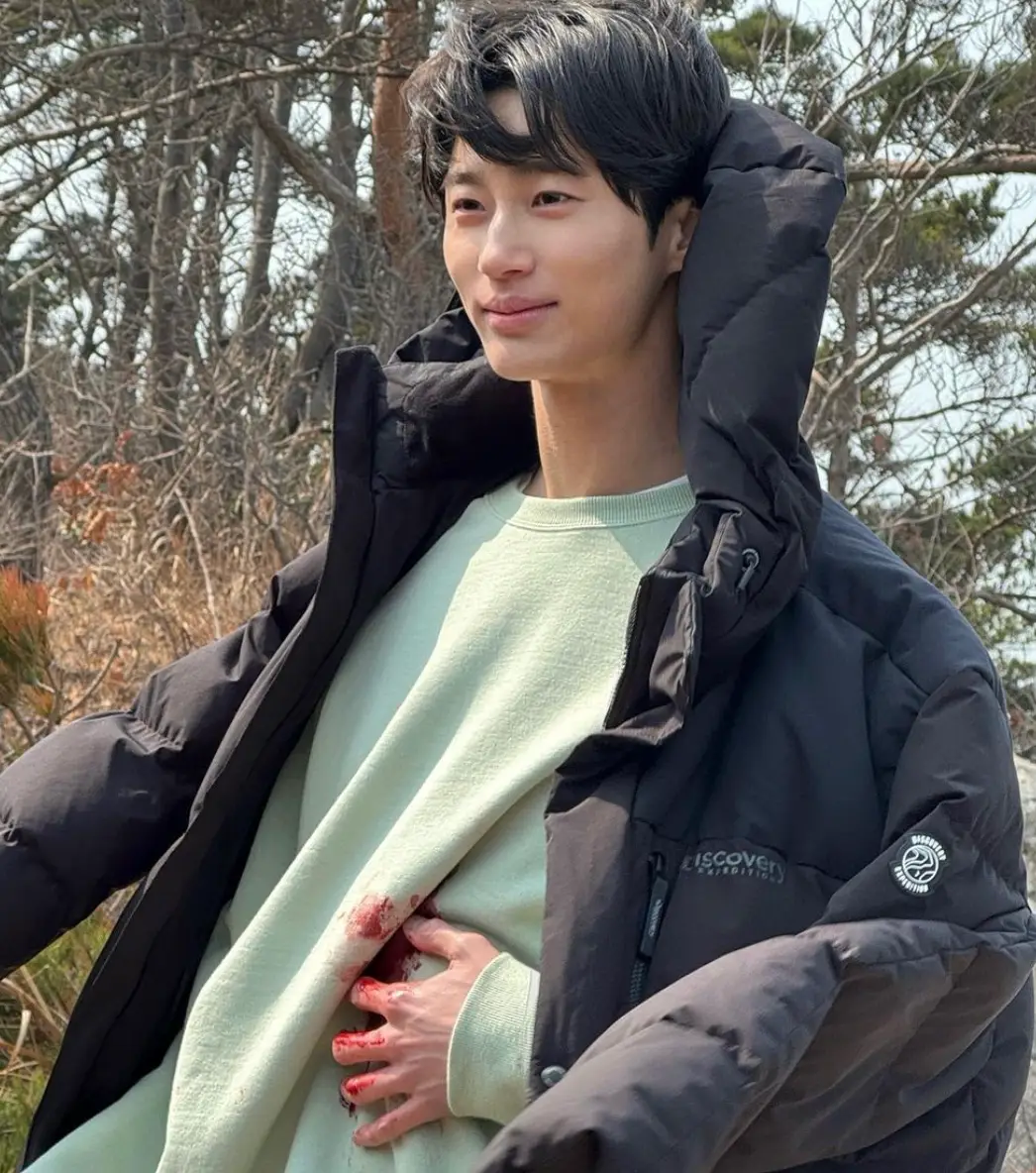 검은 잠바 안 초록색 니트의 좌측 피묻은 티를 왼손으로 막고 있는 모습