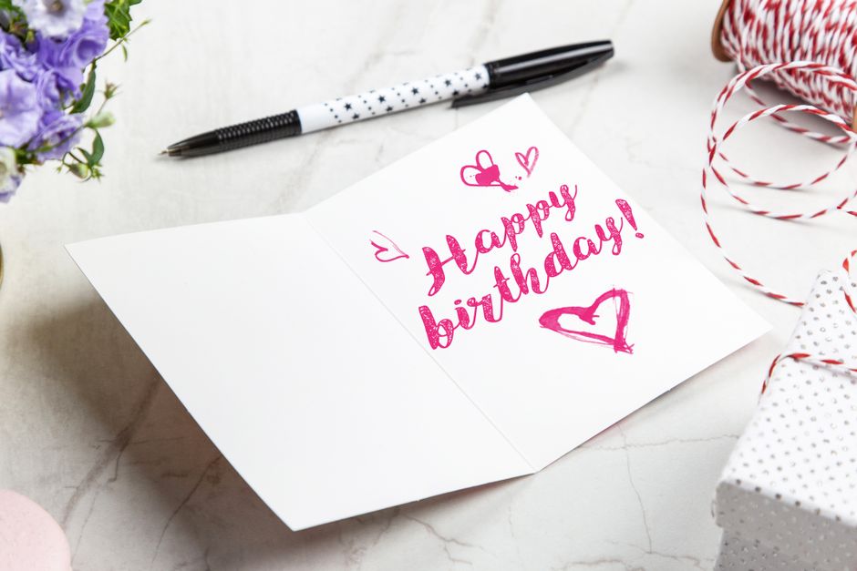 A vibrant birthday card with heart illustrations, surrounded by a pen, flowers, and gift wrap.