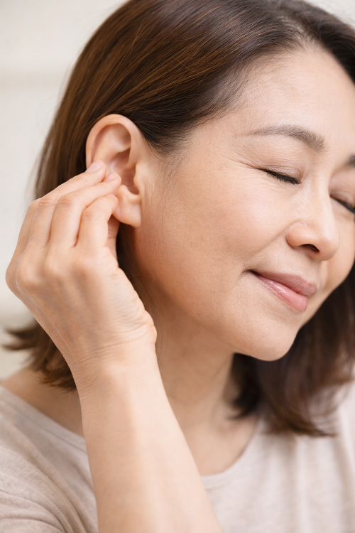 중년 여성이 귀 마사지를 하며 이혈 마사지와 귀 혈자리 자극으로 몸의 피로를 관리하는 장면