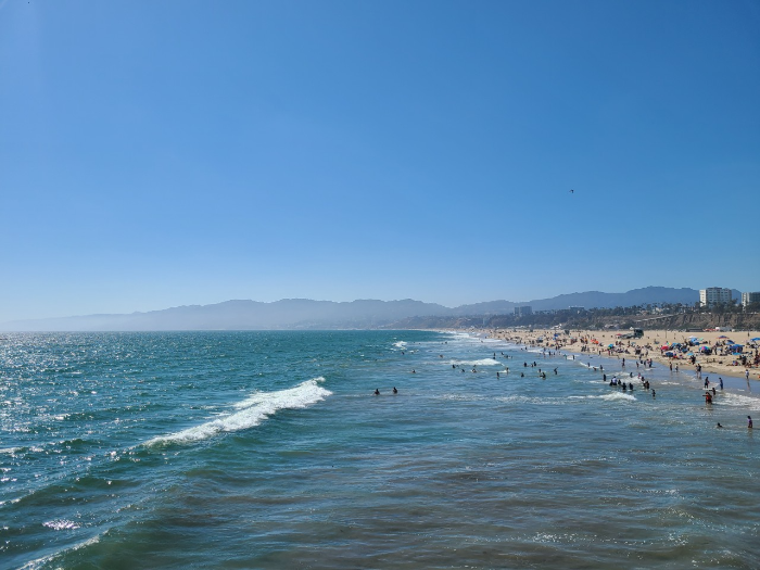 산타 모니카 피어에서 바라본 산타 모니카 해변. 왼쪽으로는 태평양의 파란 바다가 파도 치고 있다. 바다는 빛을 반사해 반짝 거린다. 오른쪽으로는 해변과 해수욕을 즐기는 사람들이 있다.