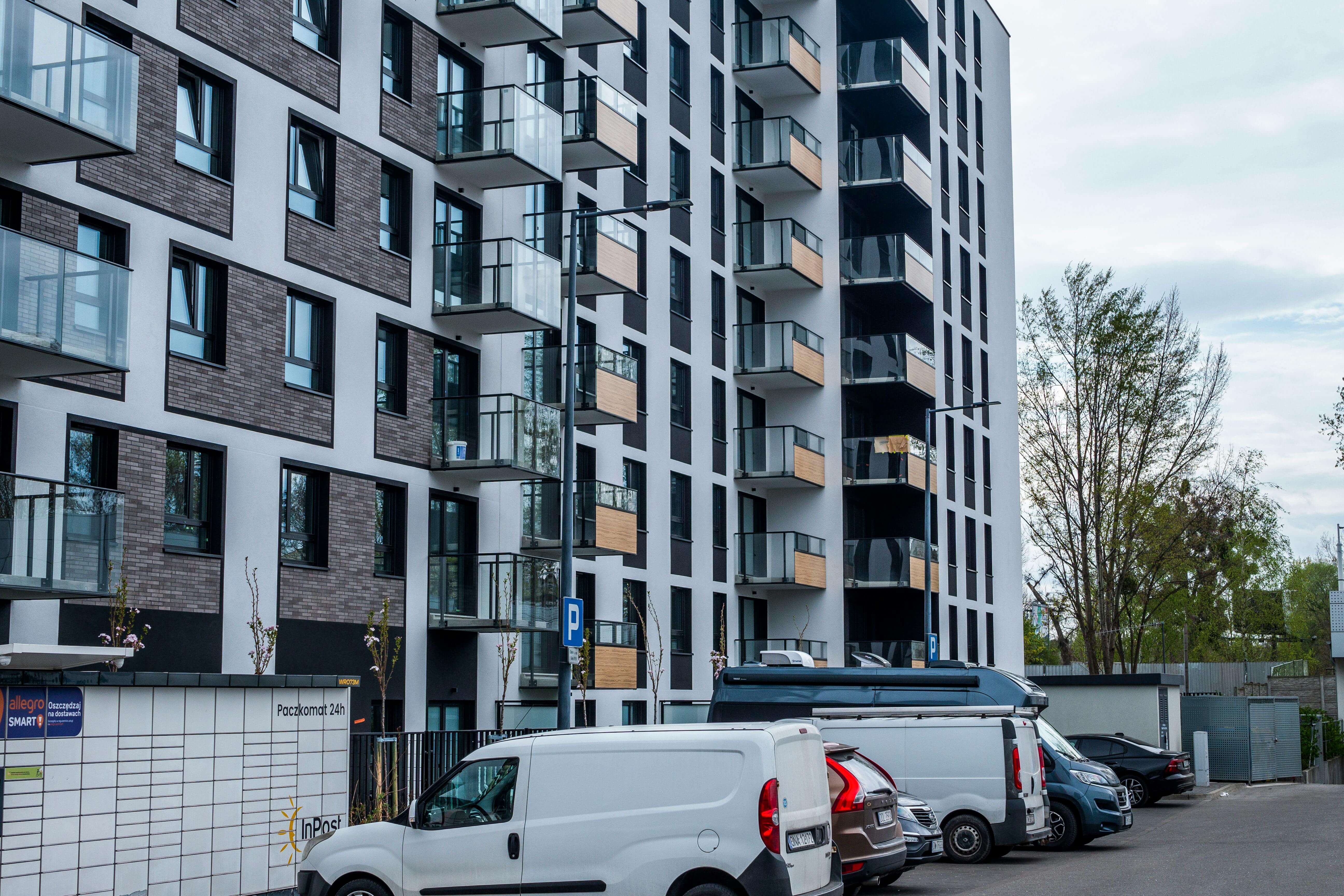 아파트 측면 돌출형 베란다가 일렬로 보이고 주차장에 차들이 여러 대 주차하고 있는 전경