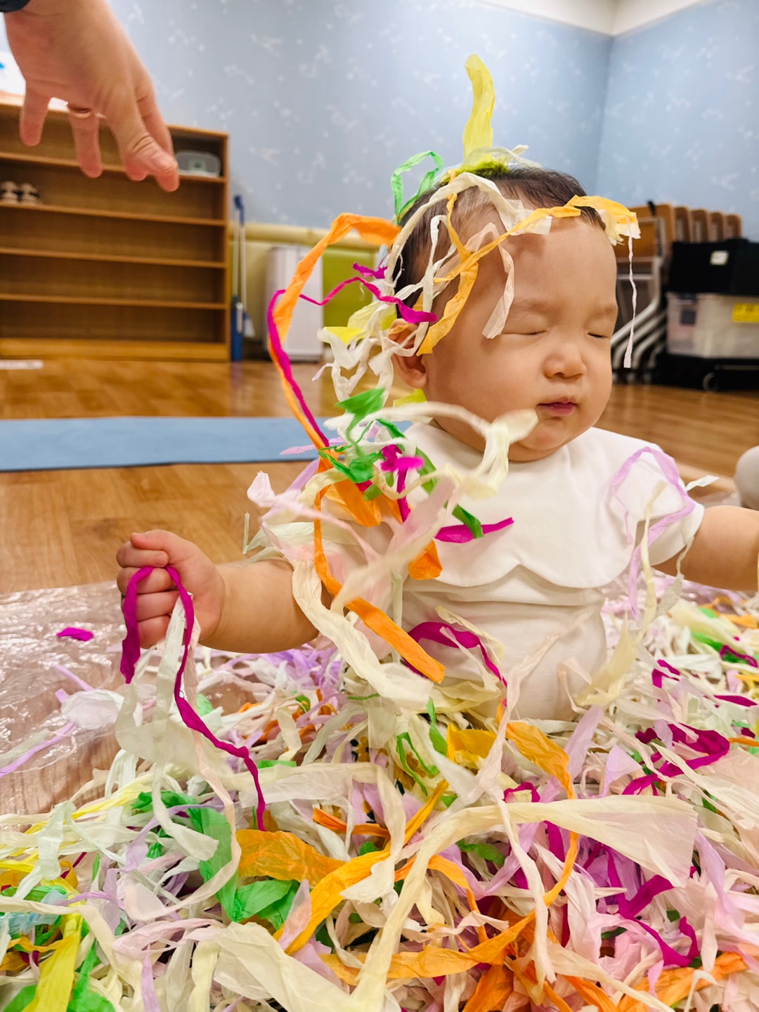 습자지를 손에 들고 머리와 어깨 위에 올려진 채 감각 놀이 중인 9개월 아기