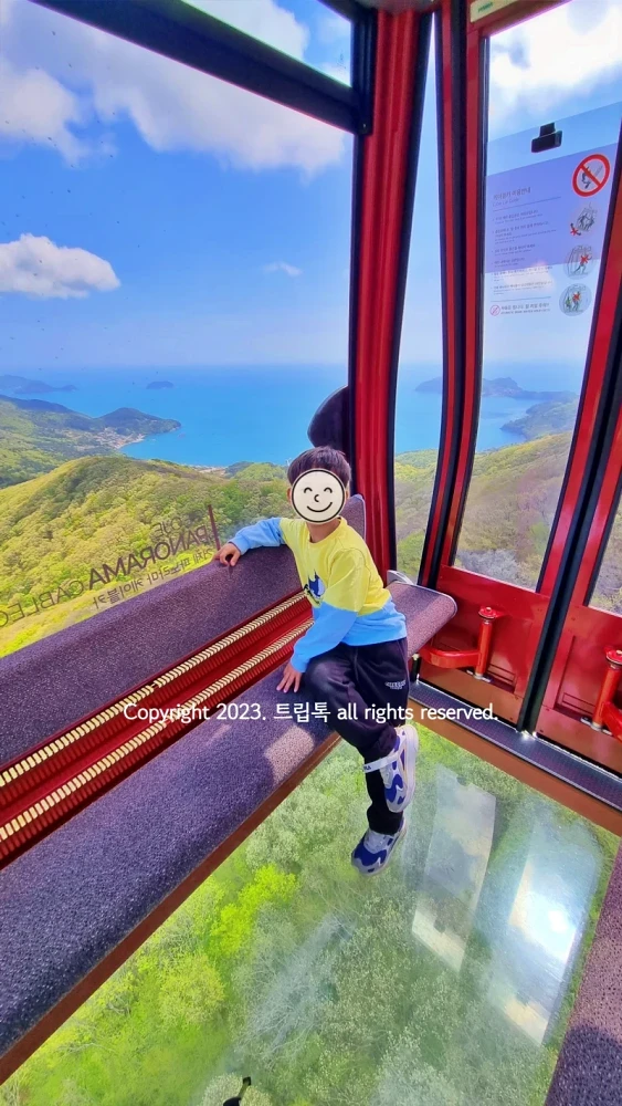 푸른하늘에 하얀 구름과 초록산과 푸른 한려해상 바다가 함께 보이는 바닥이 투명 유리로 된 케이블카에서 찍은 사진