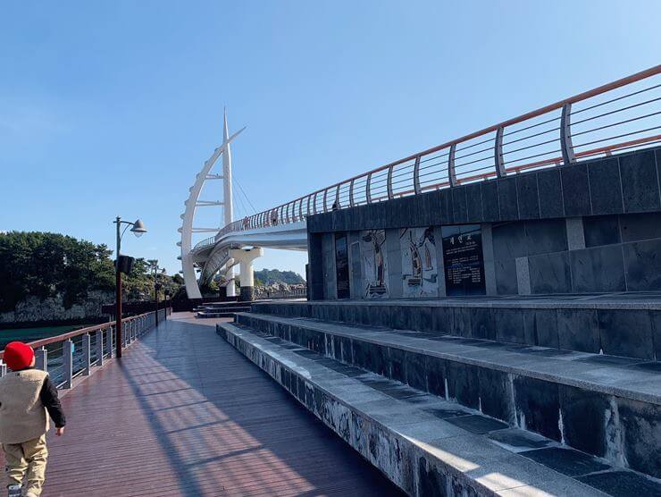 오른쪽에 새연교가 있고 왼쪽에 빨간 모자를 쓴 아이가 산책을 하고 있다.