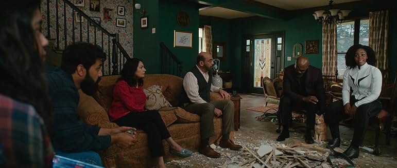 카말라 칸의 집 거실에서 가족과 모니카 램보가 대화하는 장면