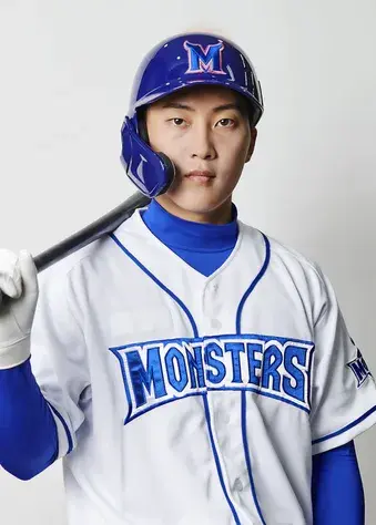 파란색 헬맷을 쓰고 야구배트를 어깨에 걸치고 남자가 서있다.