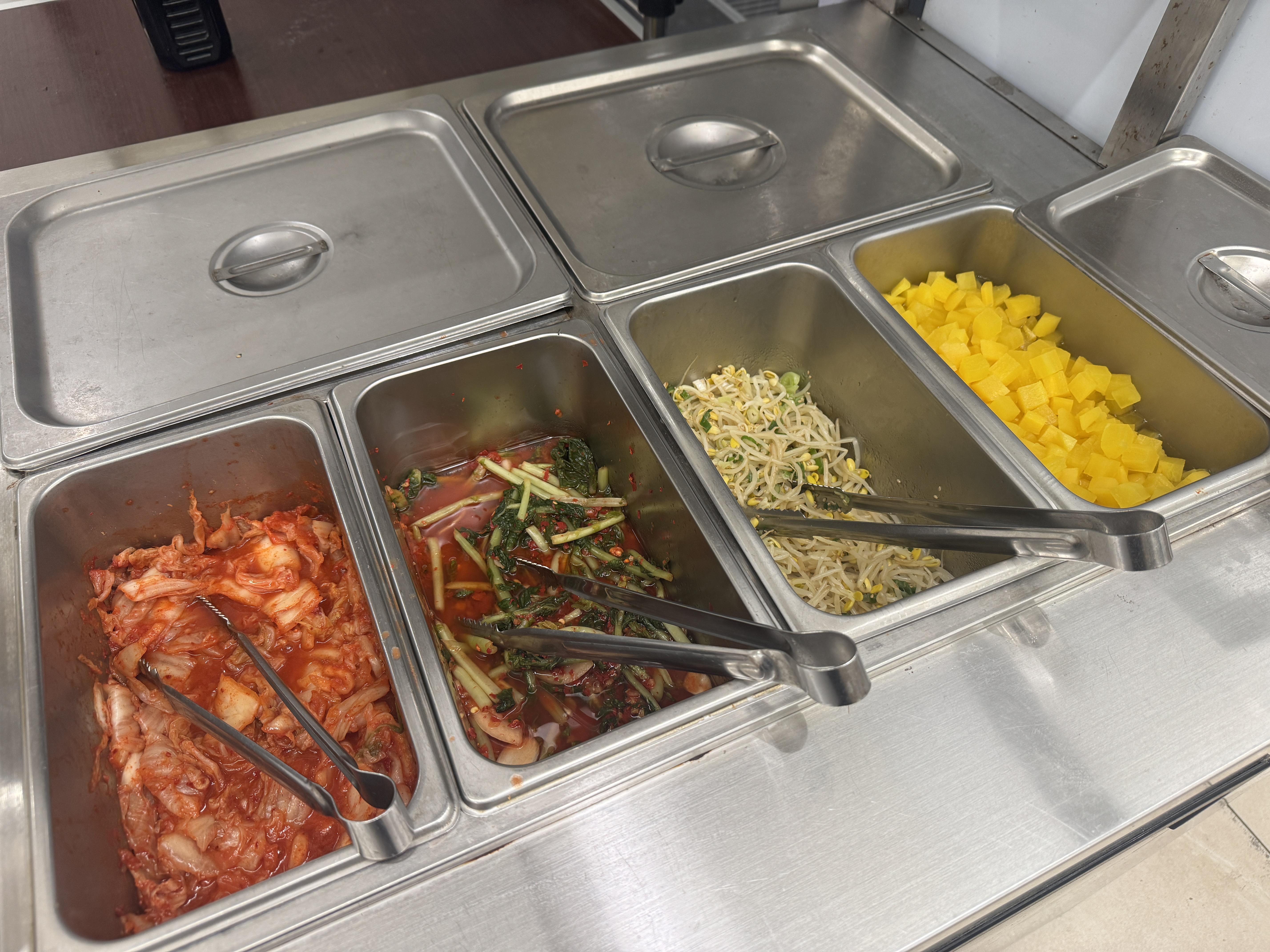 용인 수지구 동천동 바른식탁 셀프바 전경. 김치&amp;#44; 열무김치&amp;#44; 콩나물무침&amp;#44; 단무지가 스테인리스 용기에 담겨 있다.