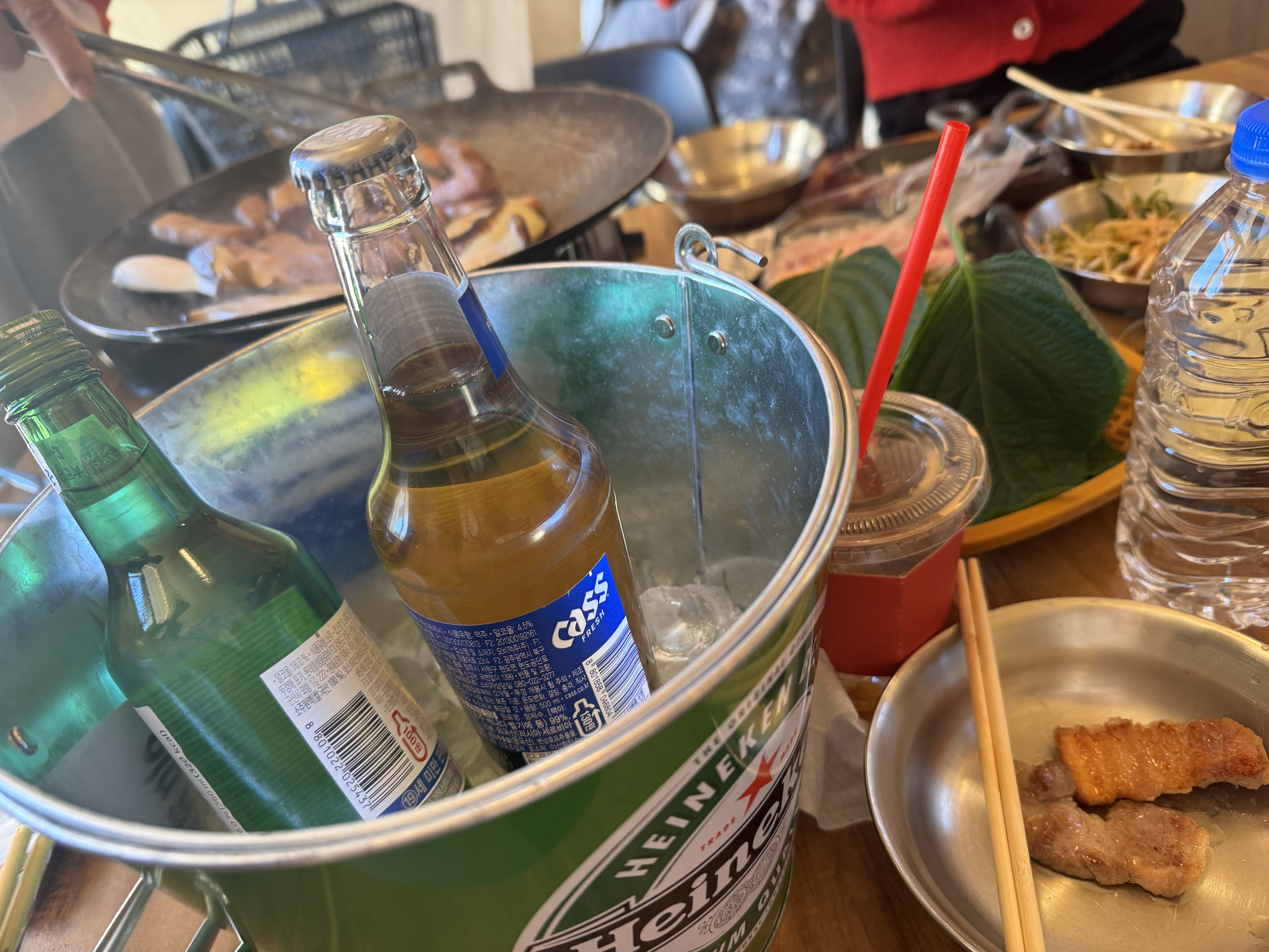 잠실 근교 셀프 바베큐장 바베큐팩토리 감북점에서 즐기는 맥주와 바베큐. 얼음으로 채워진 아이스버켓안에 참이슬과 카스 1병씩 있다. 뒤로는 고기가 구워지고 있다. 