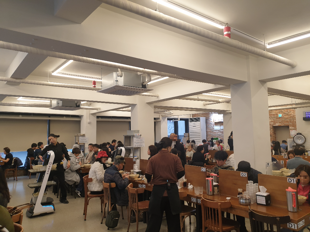 내부에 좌석들이 촘촘히 배치되어 있다. 서빙 로봇 및 직원들이 일하고 있다.