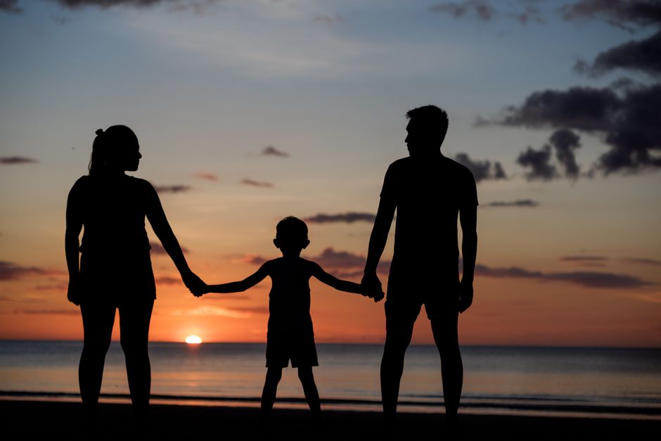 A silhouette of a family holding hands on a beach during a beautiful sunset.