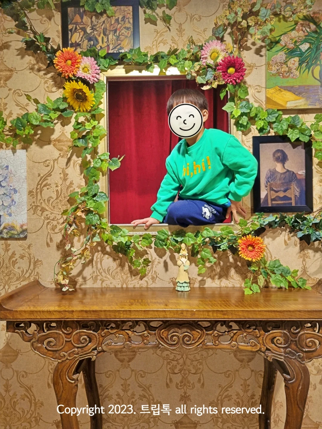 담쟁이 덩쿨과 꽃으로 둘러싸인 창문에 아이가 걸터 앉아있다