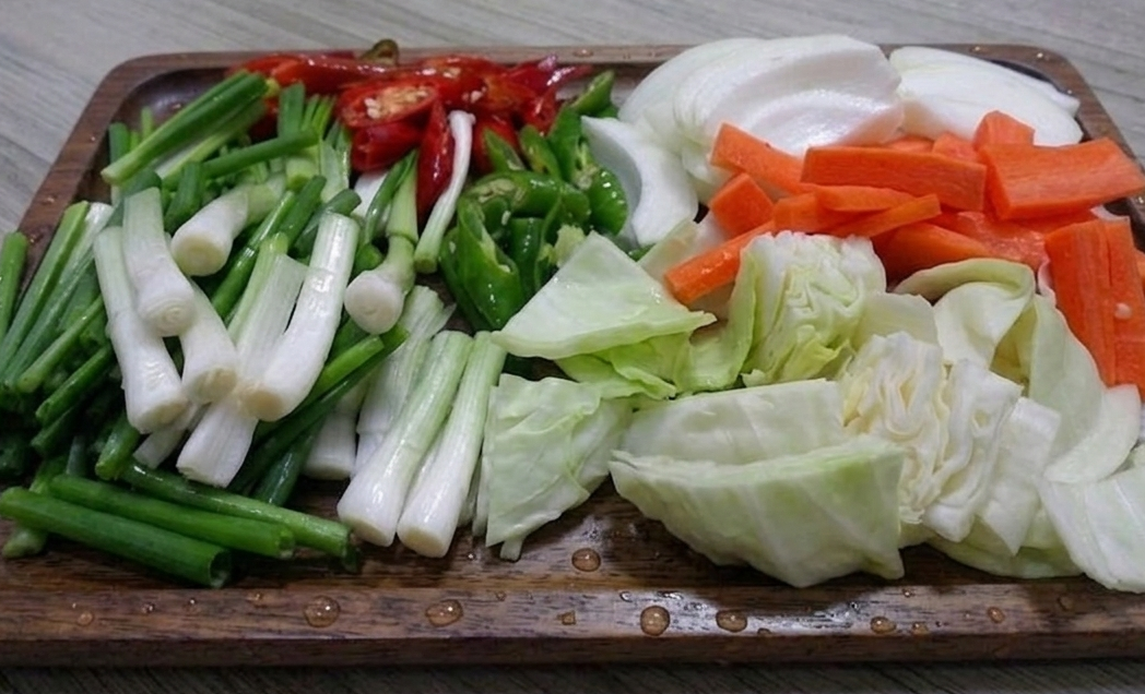 나무 트레이 위에 정갈하게 손질된 오삼불고기용 채소들(대파, 양파, 양배추, 당근, 청양고추, 홍고추).