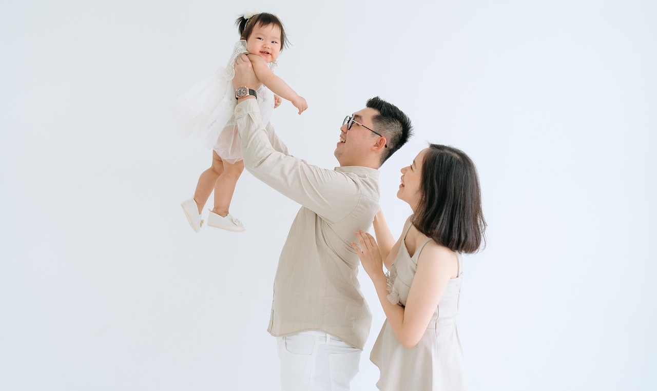 아빠가 딸을 번쩍 들고 아빠와 엄마가 딸을 바라 보고 있는 사진입니다.