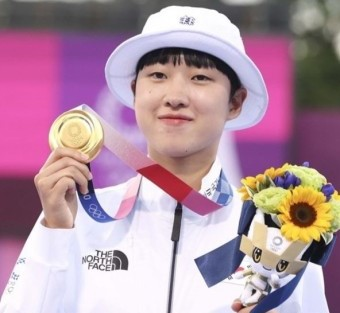 금메달을 한손에 들어올리고, 다른 한손엔 작은 꽃다발을 들고 미소짓는 안산선수 사진