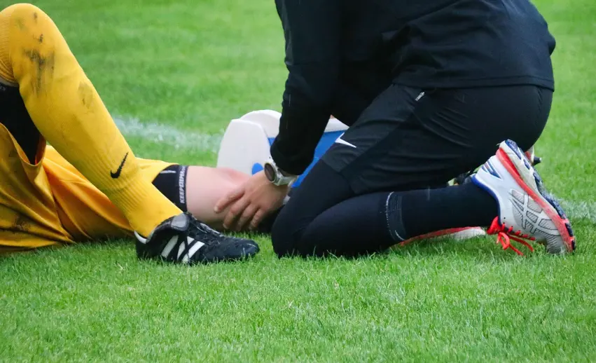 축구 경기 중 햄스트링 부상으로 쓰러진 선수와 상태를 확인하는 의료진의 응급 처치 모습
