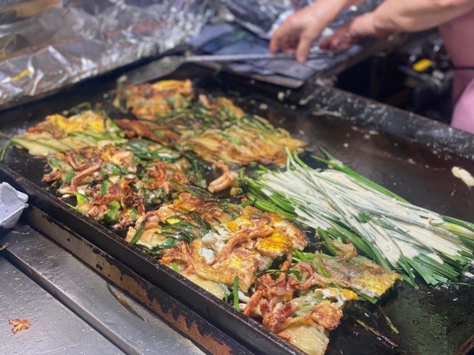 매장 입구 철판에서 직원이 파전을 직접 굽고 있는 모습. 반죽이 철판 위에서 지글지글 익어가는 장면