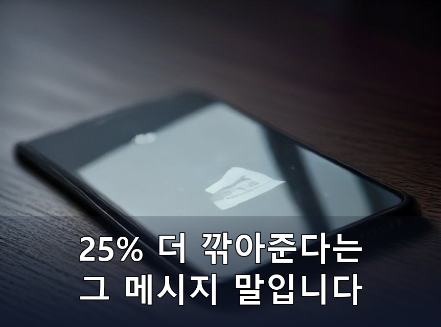 어두운 나무 책상 위에 화면이 꺼진 검은색 스마트폰 한 대가 비스듬히 놓인 클로즈업 사진. 강한 측면광에 유리와 금속 테두리 질감이 또렷하고 화면에는 읽을 수 있는 글자 없이 조명 반사만 비치며, 사진 하단 3분의 1에 짙은 네이비 띠를 깔고 그 위에 검정 테두리를 두른 흰 글씨로 두 줄 문구(25% 더 깎아준다는 / 그 메시지 말입니다)를 합성했습니다