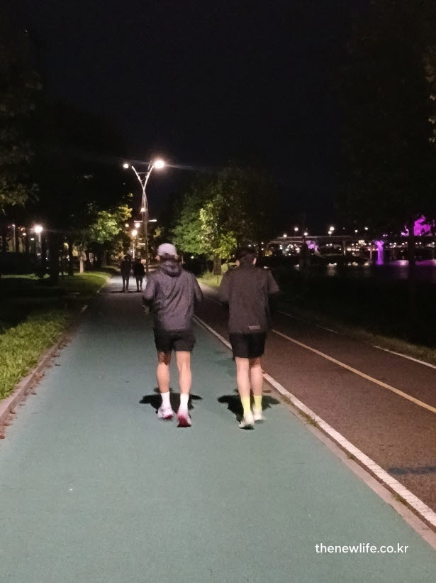 한강변 야간 코스에서 짧은 보폭과 미드풋 착지로 슬로우 조깅 방법을 실천하는 사람들의 모습