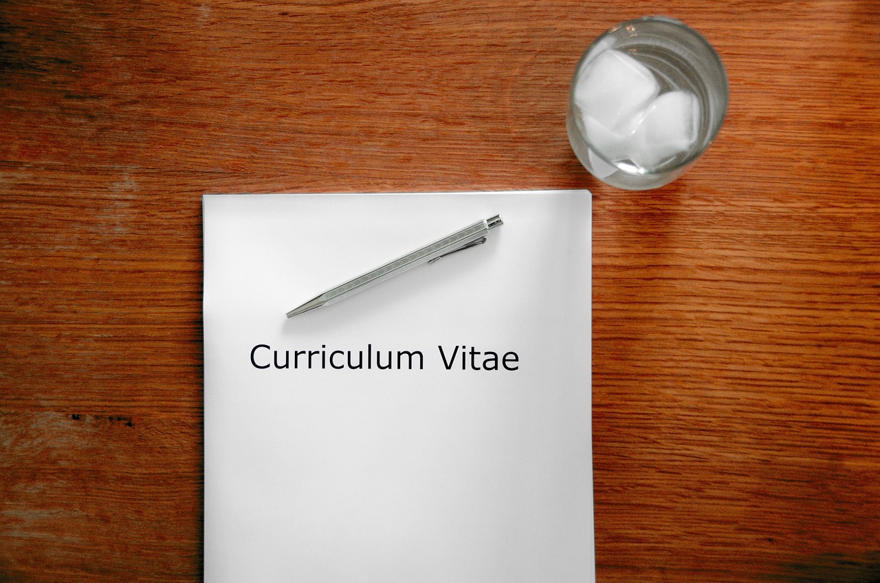 책상위에 curriculum vitae라고 써있는 종이와 펜, 물 컵이 놓여있는 사진