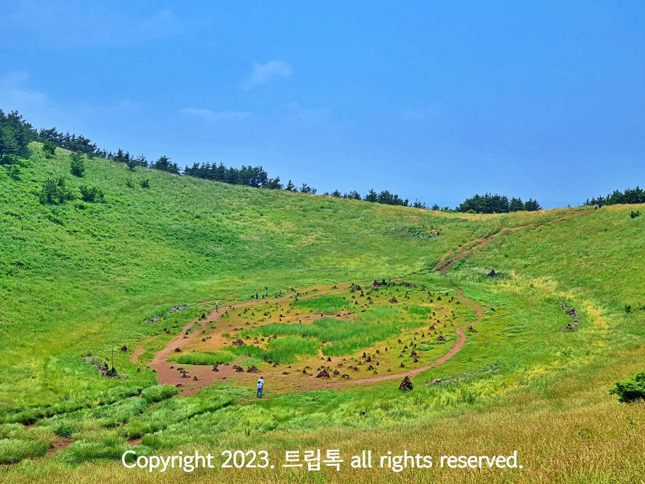 둥그런 산 정상에 움푹패인 모양이다. 안에 다양한 초록색으로 채워졌고 동그란 흙길과 점같은 돌이 보인다.