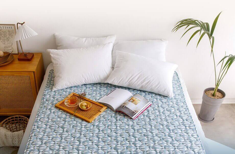 베개 4개와 쟁반 위 접시가 놓여있고 책이 펼쳐져 있는 침대